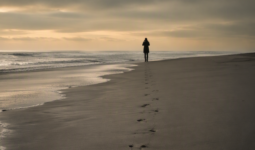 A lone figure standing at the edge of an empty beach at dusk